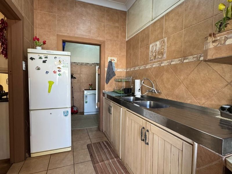 A functional scullery featuring a stainless steel countertop with a double basin sink, tiled walls, and built-in wooden cabinetry.