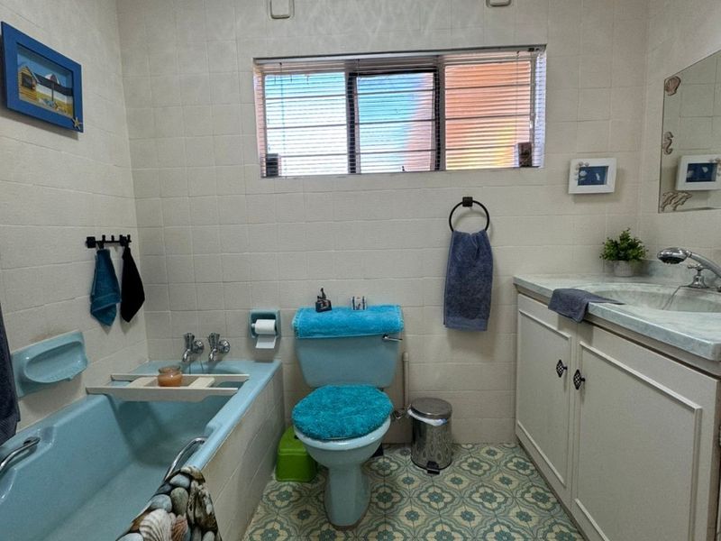 A dated bathroom featuring a blue bathtub and toilet, patterned floor tiles, and a built-in vanity cabinet with a basin.