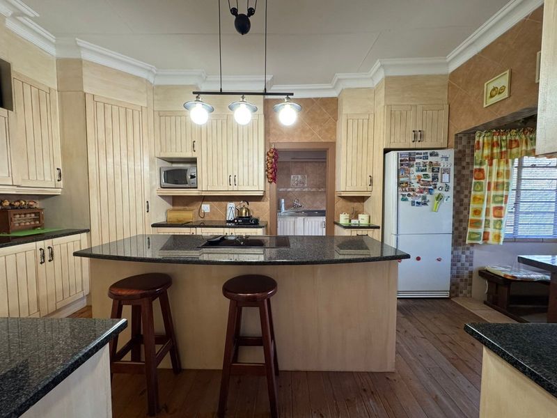 A functional kitchen featuring a central island with a granite countertop, built-in cabinetry, and an integrated hob, with an adjoining scullery area.