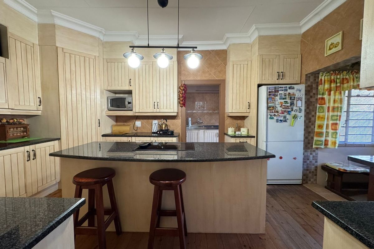 A functional kitchen featuring a central island with a granite countertop, built-in cabinetry, and an integrated hob, with an adjoining scullery area.