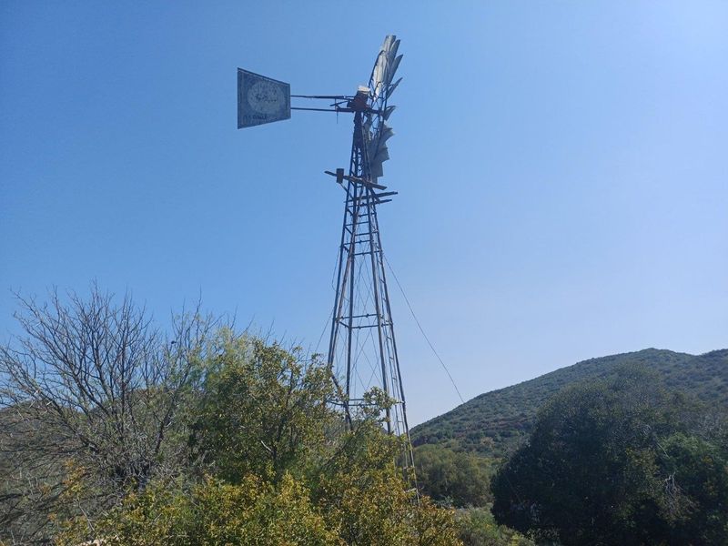 A traditional metal farm windmill used for water pumping, situated in a rural landscape setting.