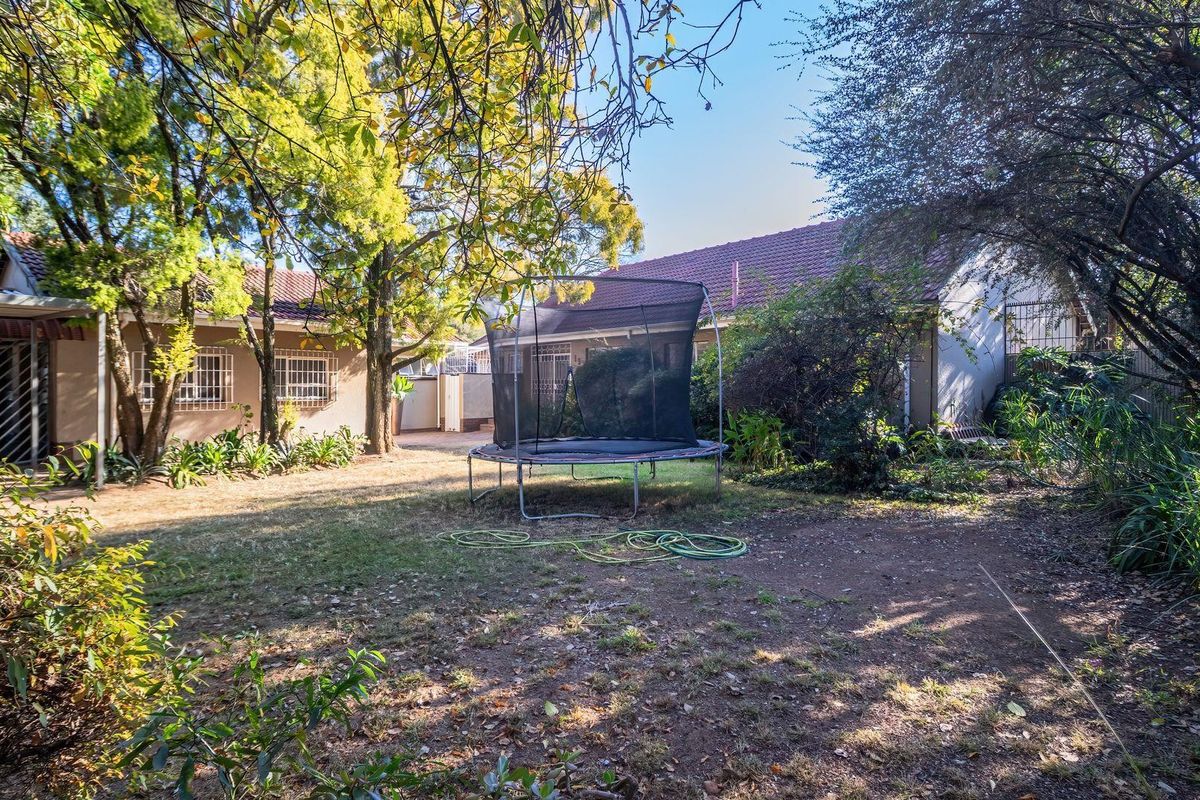 A view of the rear garden area featuring mature trees, a lawn, and the rear facade of the house with security bars on windows.