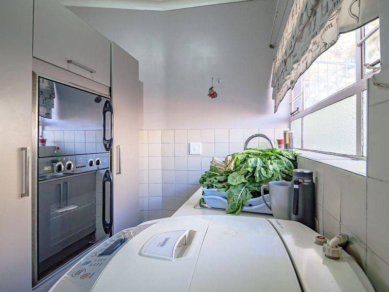 A functional laundry area featuring built-in cabinetry, a wall-mounted oven, and tiled splashbacks with a window for natural light.
