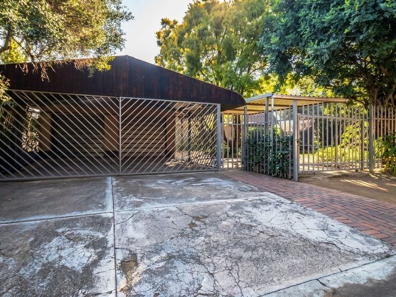 Front exterior view featuring a metal security gate, carport structure, and a concrete driveway with visible surface cracking.