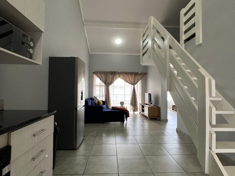 Open-plan living area featuring tiled flooring, a modern staircase, and a functional kitchen layout with built-in cabinetry and appliances.