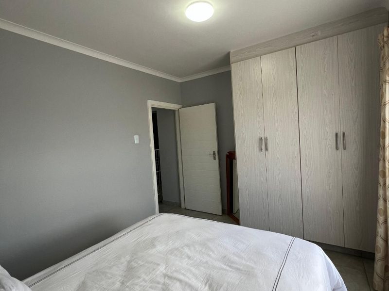 A well-maintained bedroom featuring neutral grey walls, tiled flooring, and ample built-in cupboard storage.