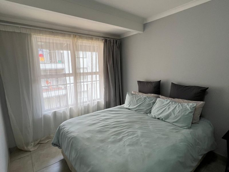 A well-maintained bedroom featuring neutral grey walls, tiled flooring, and a large window with curtain tracks.