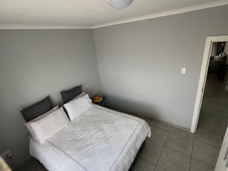 A bedroom featuring neutral grey walls, tiled flooring, and a central ceiling light fixture, providing a clean and functional living space.