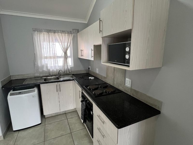 A functional kitchen featuring light wood-finish cabinetry, dark granite countertops, built-in oven and hob, and tiled flooring.