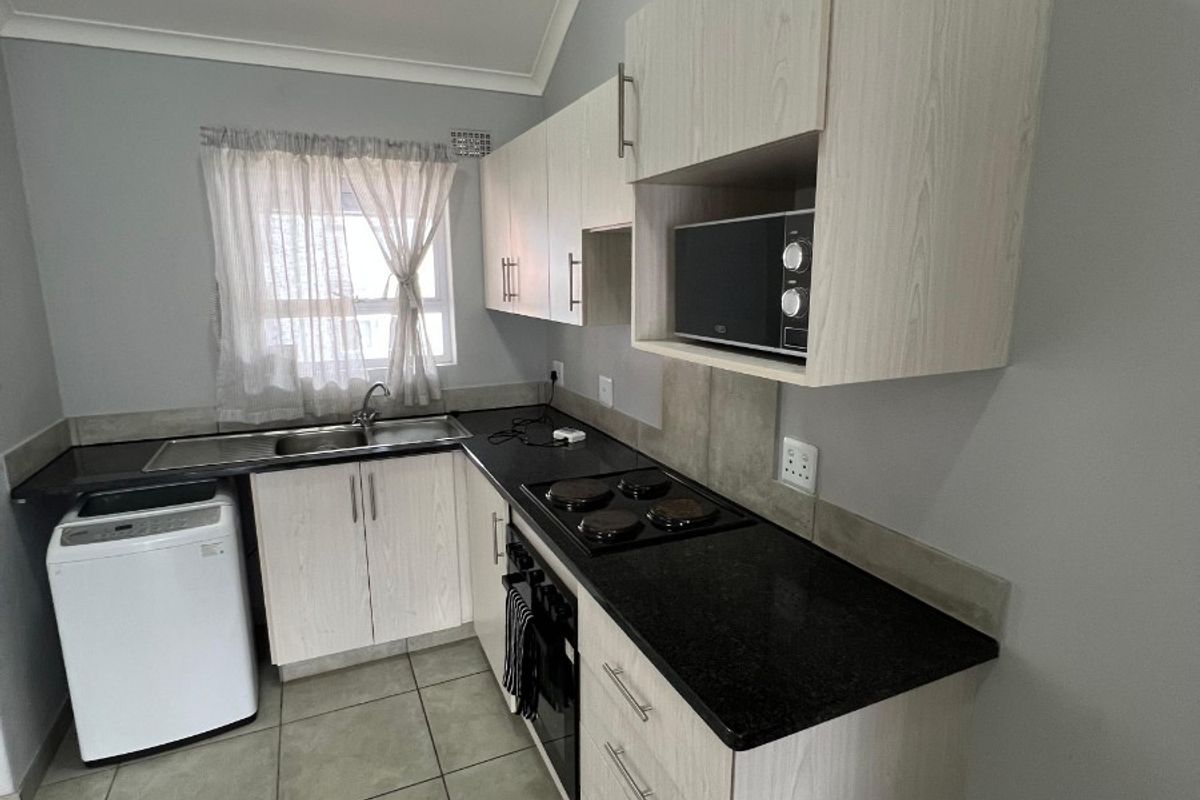 A functional kitchen featuring light wood-finish cabinetry, dark granite countertops, built-in oven and hob, and tiled flooring.