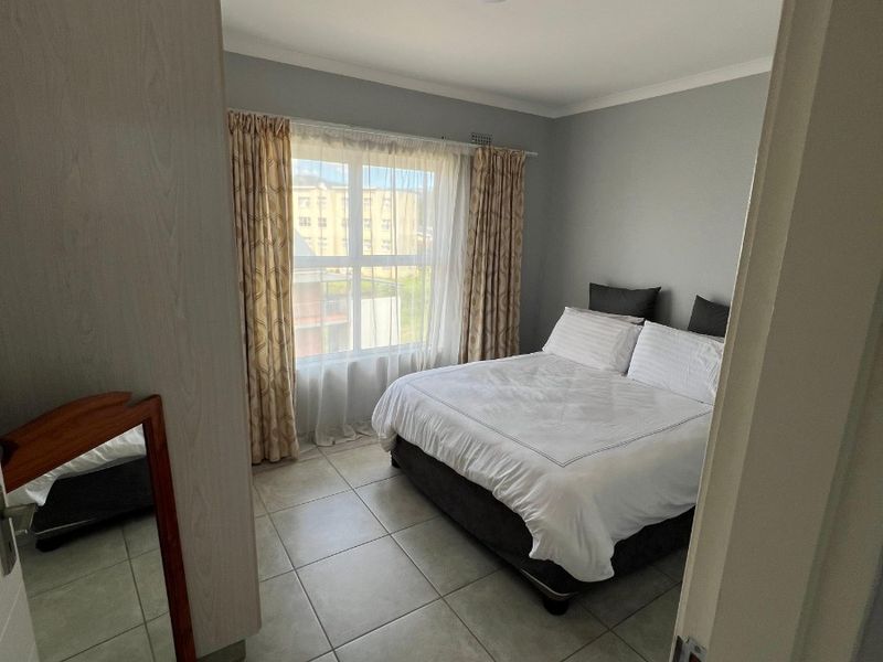 A well-maintained bedroom featuring neutral grey walls, tiled flooring, and a built-in wardrobe, offering a clean and functional living space.