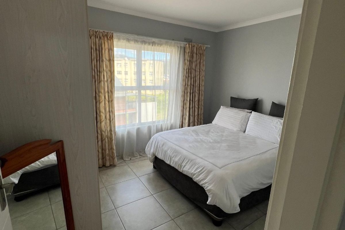 A well-maintained bedroom featuring neutral grey walls, tiled flooring, and a built-in wardrobe, offering a clean and functional living space.
