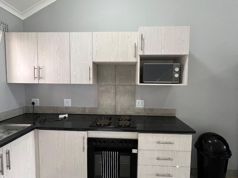 Modern kitchen featuring light wood-grain cabinetry, dark granite countertops, built-in oven and hob, and neutral tiled flooring with a vaulted ceiling.