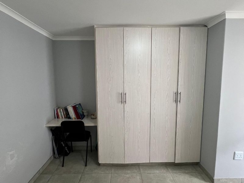 Bedroom featuring a light wood-finish built-in wardrobe with an integrated desk area and neutral tiled flooring.