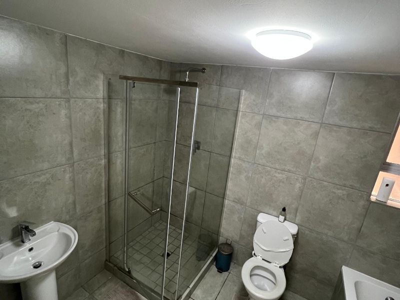 A functional bathroom featuring a pedestal basin, glass shower enclosure, toilet, and bathtub with neutral grey wall and floor tiling.
