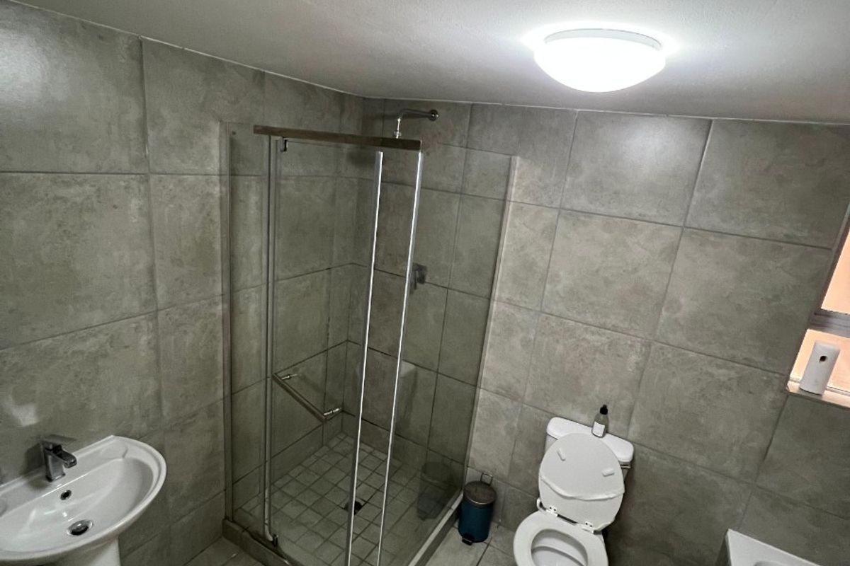 A functional bathroom featuring a pedestal basin, glass shower enclosure, toilet, and bathtub with neutral grey wall and floor tiling.
