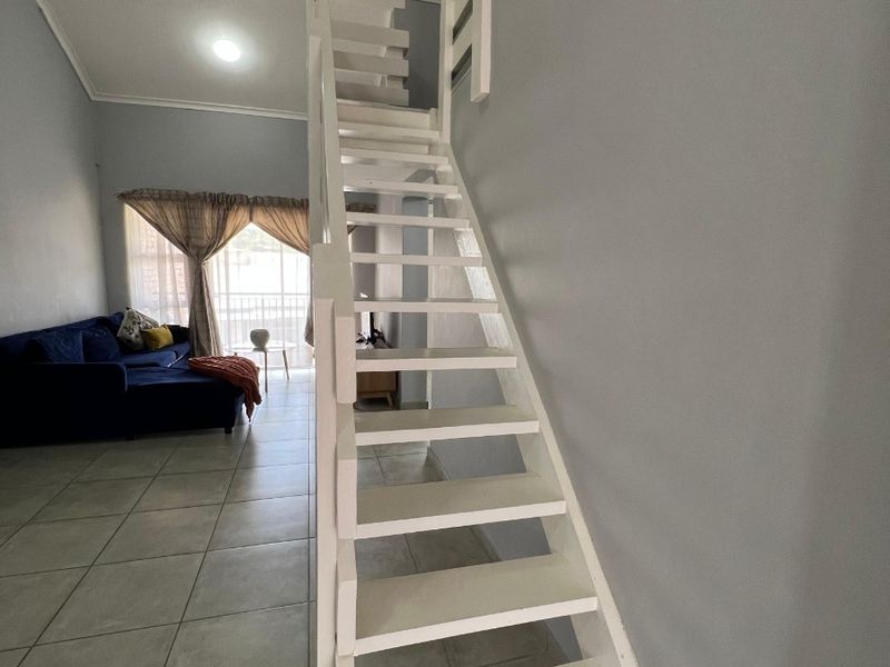 Open plan living area featuring a white staircase leading to a mezzanine level, tiled flooring, and access to a balcony.
