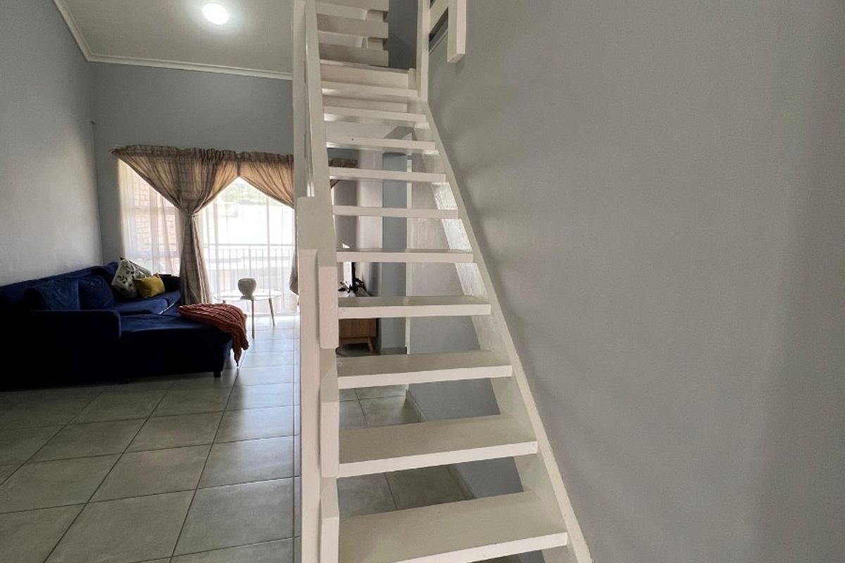 Open plan living area featuring a white staircase leading to a mezzanine level, tiled flooring, and access to a balcony.
