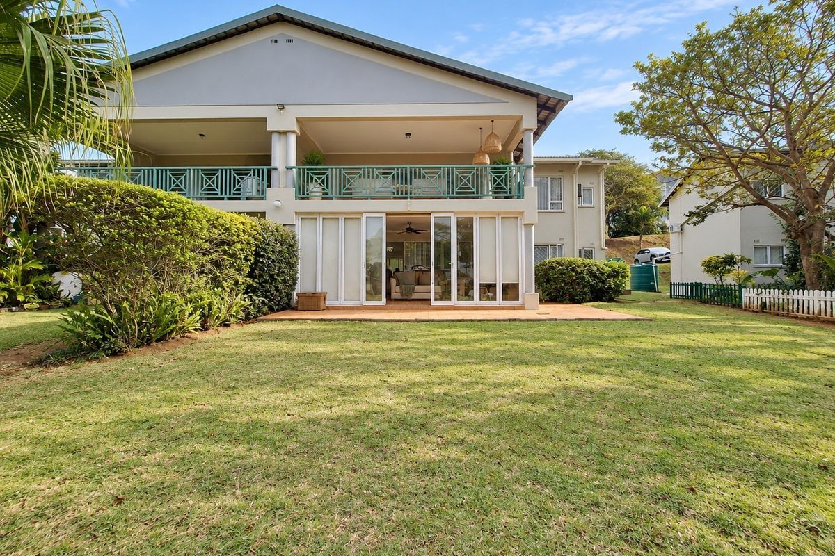 Rear view of the apartment building featuring a spacious ground floor patio with sliding doors and an upper-level balcony overlooking a private garden.