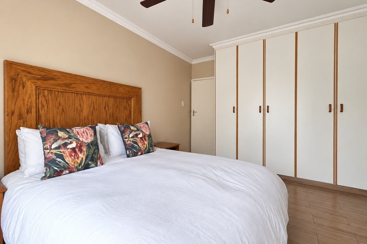 A well-maintained bedroom featuring built-in cupboards, laminate flooring, and a ceiling fan, offering a clean and functional living space.
