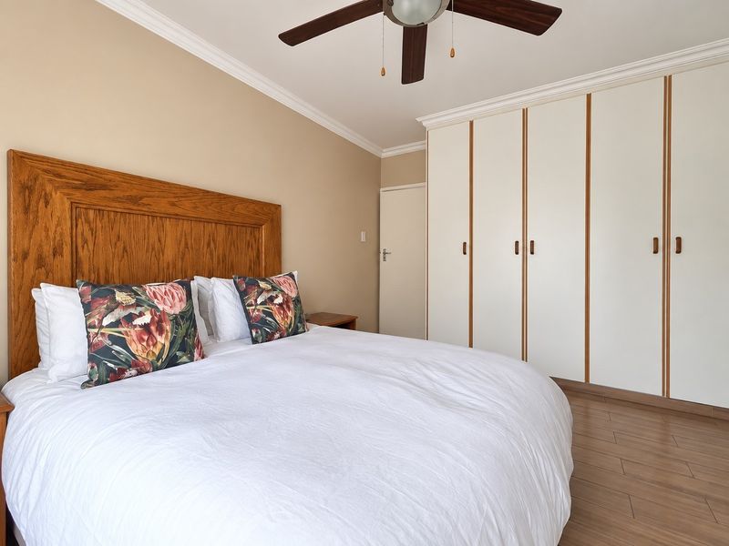 A well-maintained bedroom featuring built-in cupboards, laminate flooring, and a ceiling fan, offering a clean and functional living space.