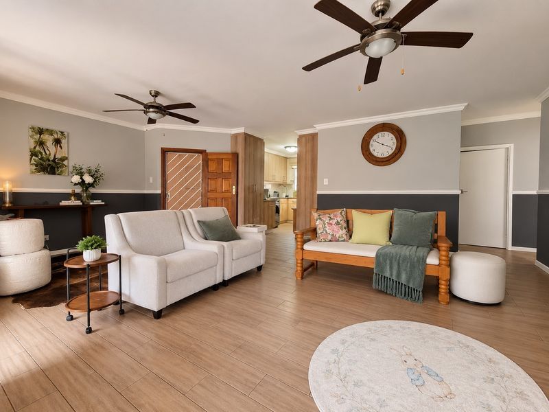 Spacious open-plan living area featuring wood-look tile flooring, dual ceiling fans, and crown molding, with a view into the adjacent kitchen.