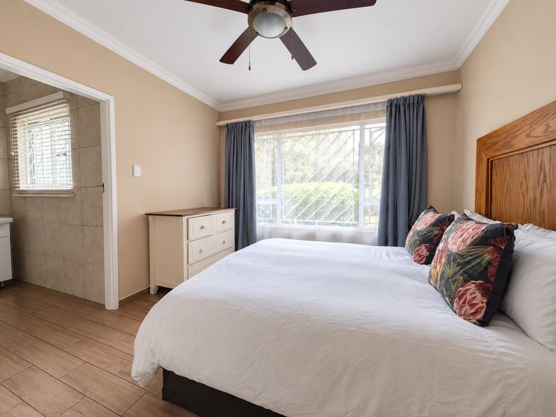 A well-maintained bedroom featuring tiled flooring, a ceiling fan, and an adjoining bathroom, with natural light through a window with security bars.