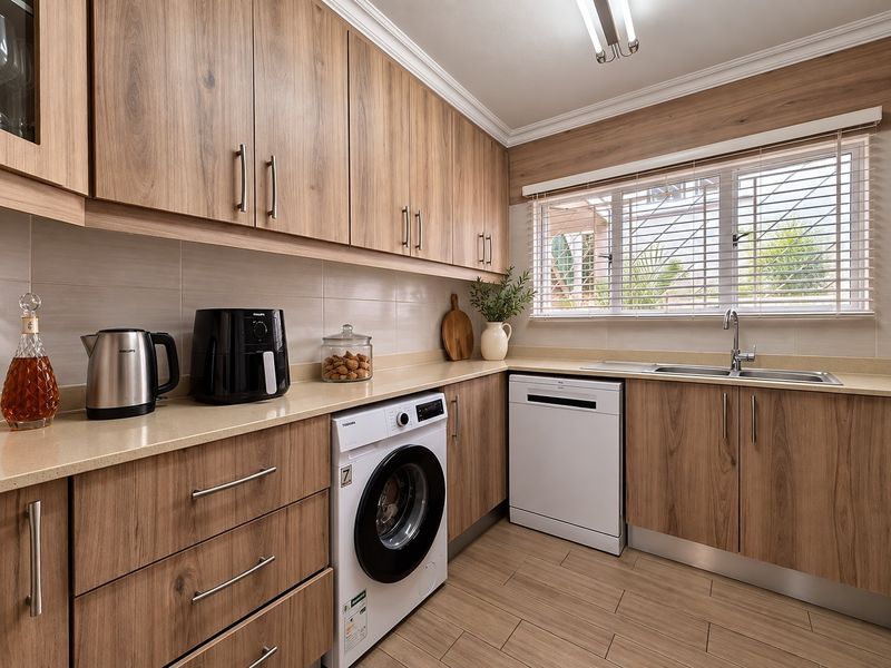A well-maintained kitchen featuring wood-look cabinetry, stone countertops, a stainless steel sink, and integrated space for laundry and dishwashing appliances.