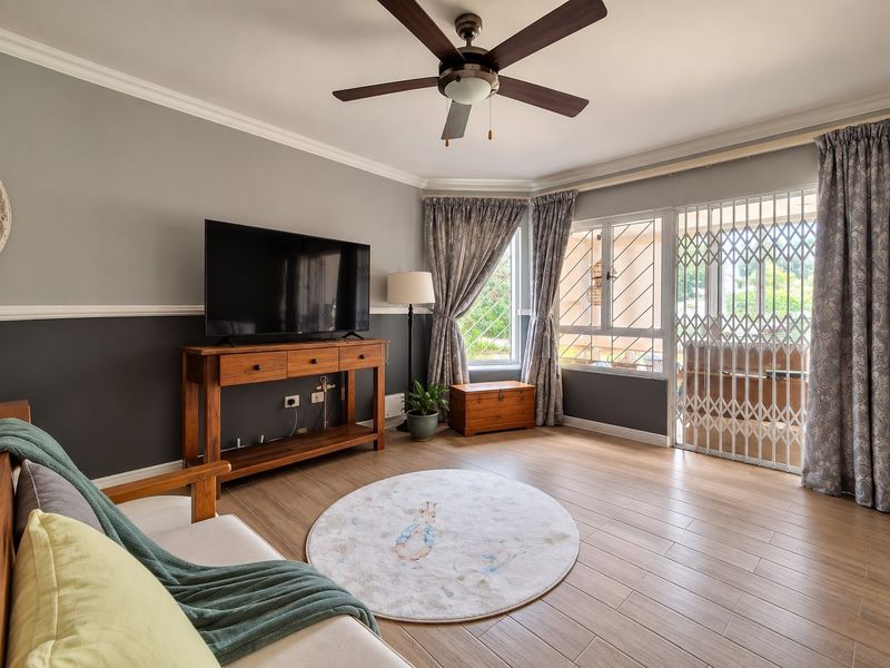 A well-maintained living room featuring laminate flooring, a ceiling fan, and secure access to an outdoor area via a sliding door with security gate.