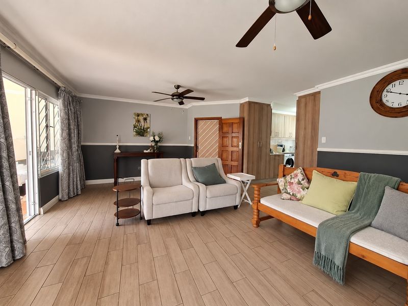 Spacious open-plan living area featuring wood-look tiled flooring, ceiling fans, and direct access to an outdoor patio through sliding glass doors.