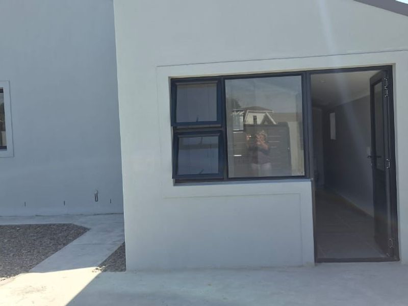 Rear exterior view of the property featuring modern grey rendered walls, dark aluminium window frames, and a paved pathway leading to the entrance.