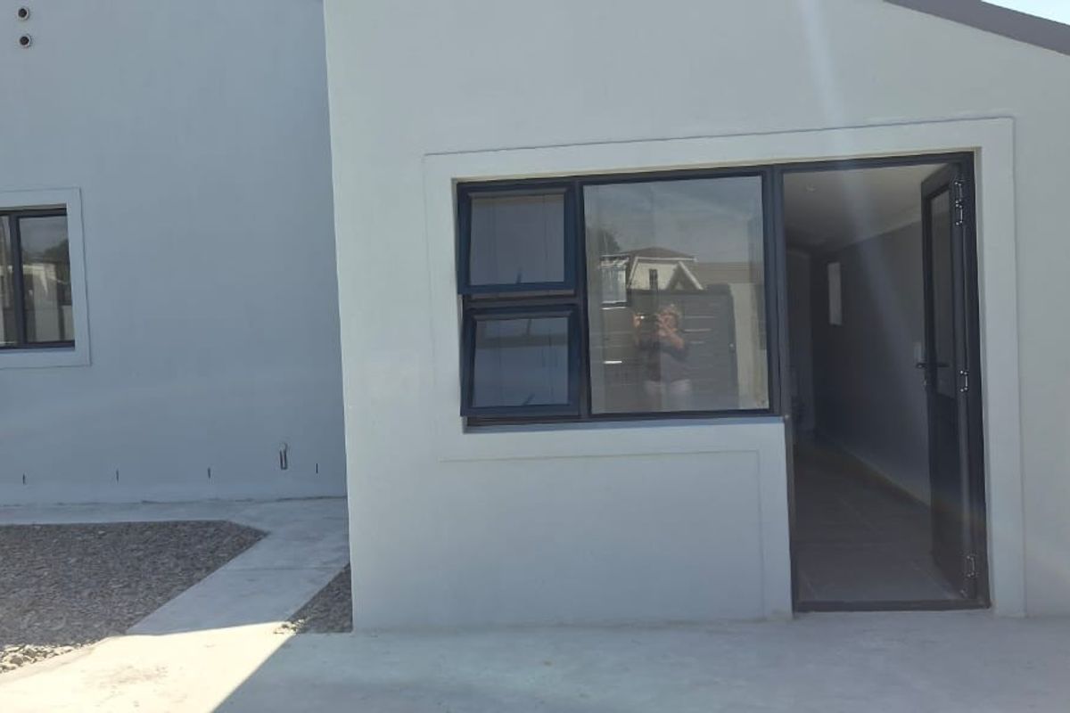 Rear exterior view of the property featuring modern grey rendered walls, dark aluminium window frames, and a paved pathway leading to the entrance.