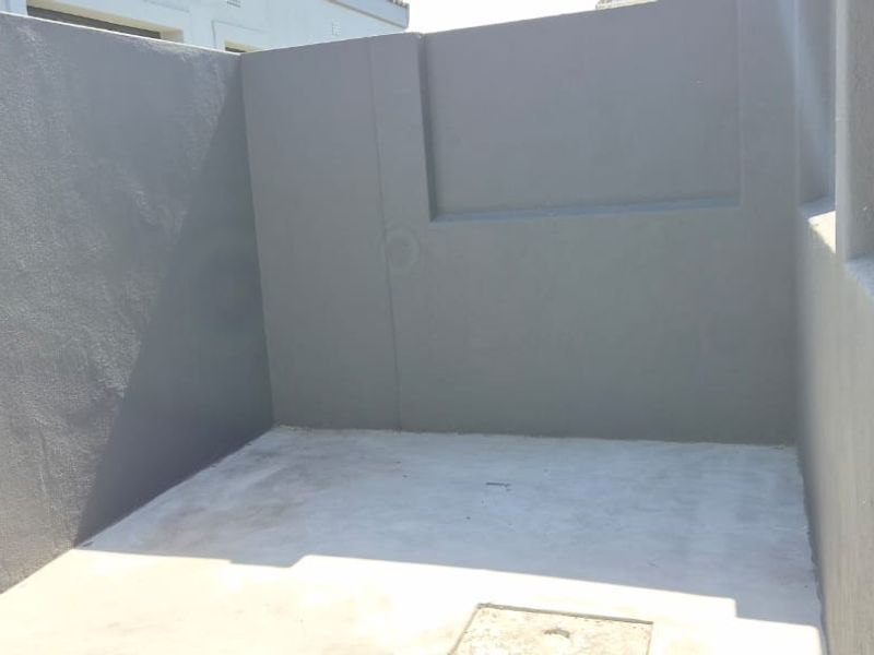 A clean, paved utility or service area featuring freshly painted grey masonry walls and a functional drainage point.