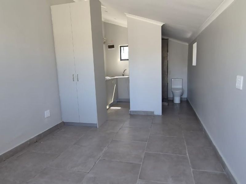 An open-plan studio space featuring tiled flooring, built-in cupboards, and a compact kitchenette and bathroom area.