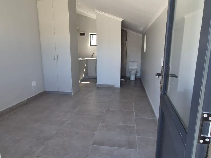 An open-plan studio space featuring tiled flooring, built-in cupboards, and a compact kitchenette with an integrated bathroom area.