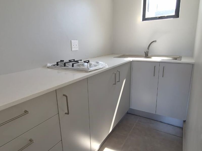 A compact, modern kitchen featuring light grey cabinetry, stone countertops, a stainless steel sink, and a built-in gas hob.
