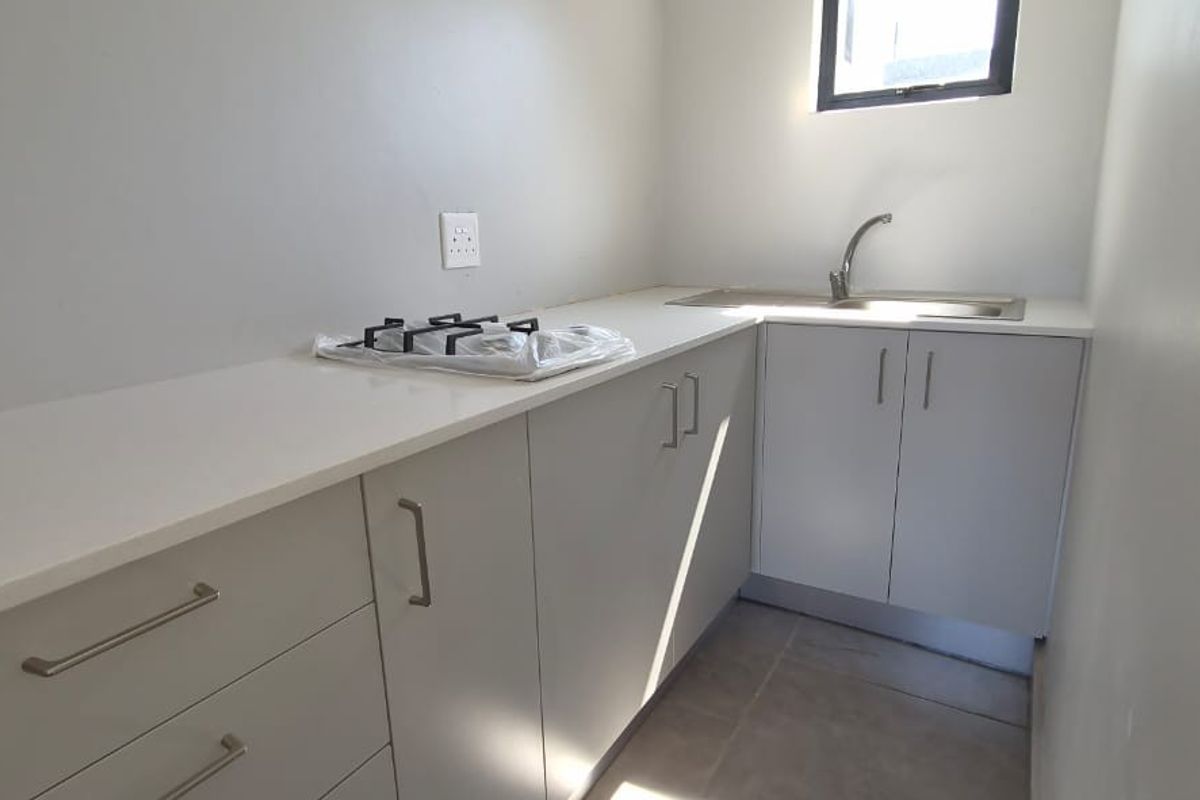 A compact, modern kitchen featuring light grey cabinetry, stone countertops, a stainless steel sink, and a built-in gas hob.