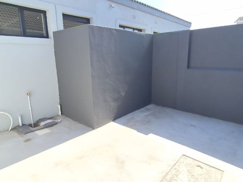A clean, paved rear courtyard area featuring a boundary wall and external plumbing connection point.