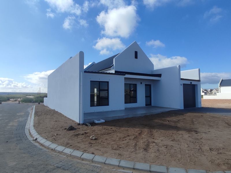 Modern single-story house with a gabled roof, aluminum window frames, and an integrated garage, situated in a developing residential area.