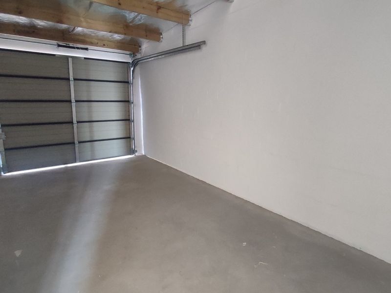 A clean, empty single-car garage featuring a sectional door, exposed timber ceiling beams, and smooth concrete flooring.
