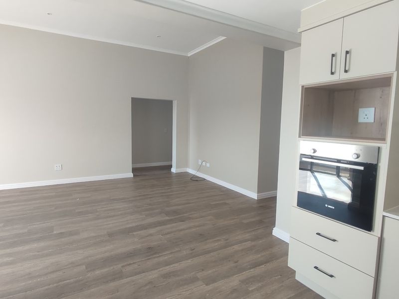 An open-plan living area featuring modern laminate flooring, neutral walls, and a compact kitchen unit with a built-in oven.