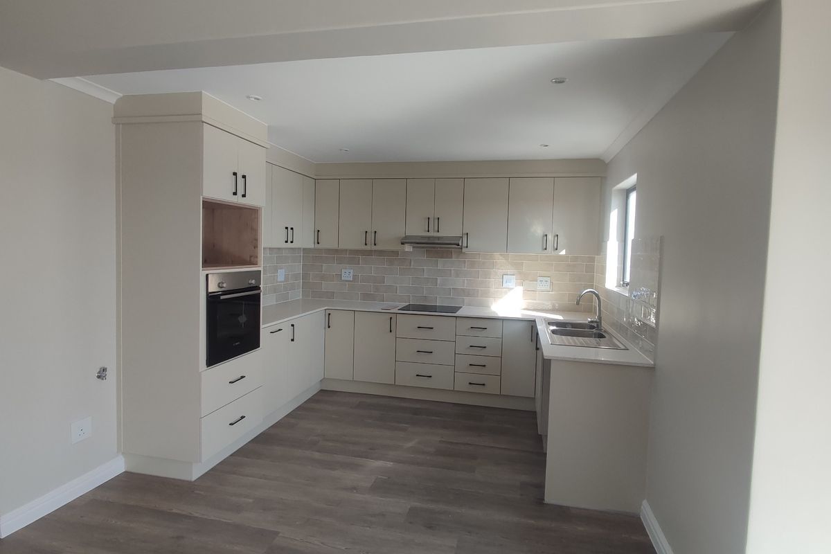 A modern, clean kitchen featuring neutral cabinetry, built-in appliances, a tiled backsplash, and durable laminate flooring in an open-plan layout.