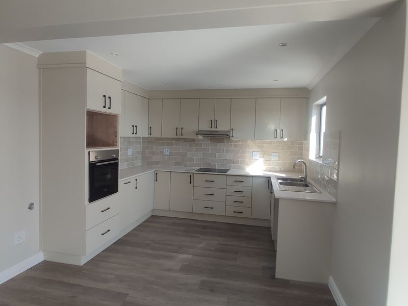 A modern, clean kitchen featuring neutral cabinetry, built-in appliances, a tiled backsplash, and durable laminate flooring in an open-plan layout.