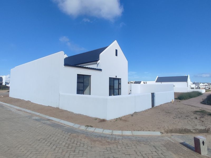 A modern white house with a dark metal roof, featuring a surrounding boundary wall and paved driveway in a new residential development.