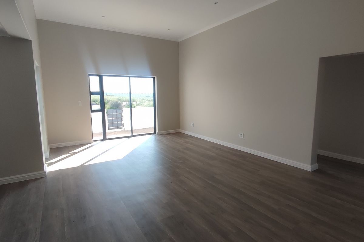 A spacious, empty living room featuring modern laminate flooring, neutral walls, recessed lighting, and a sliding glass door providing natural light and outdoor access.