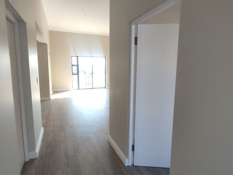 A bright, modern hallway featuring neutral walls, laminate flooring, and clean architectural lines leading into an open-plan living area with sliding glass doors.