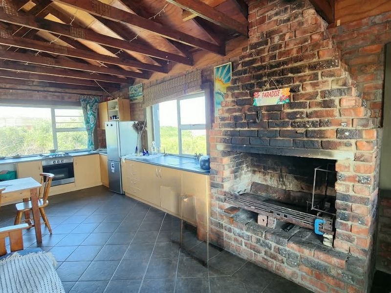 Open-plan living and kitchen area featuring a rustic exposed timber ceiling, tiled floors, and a prominent built-in brick fireplace.