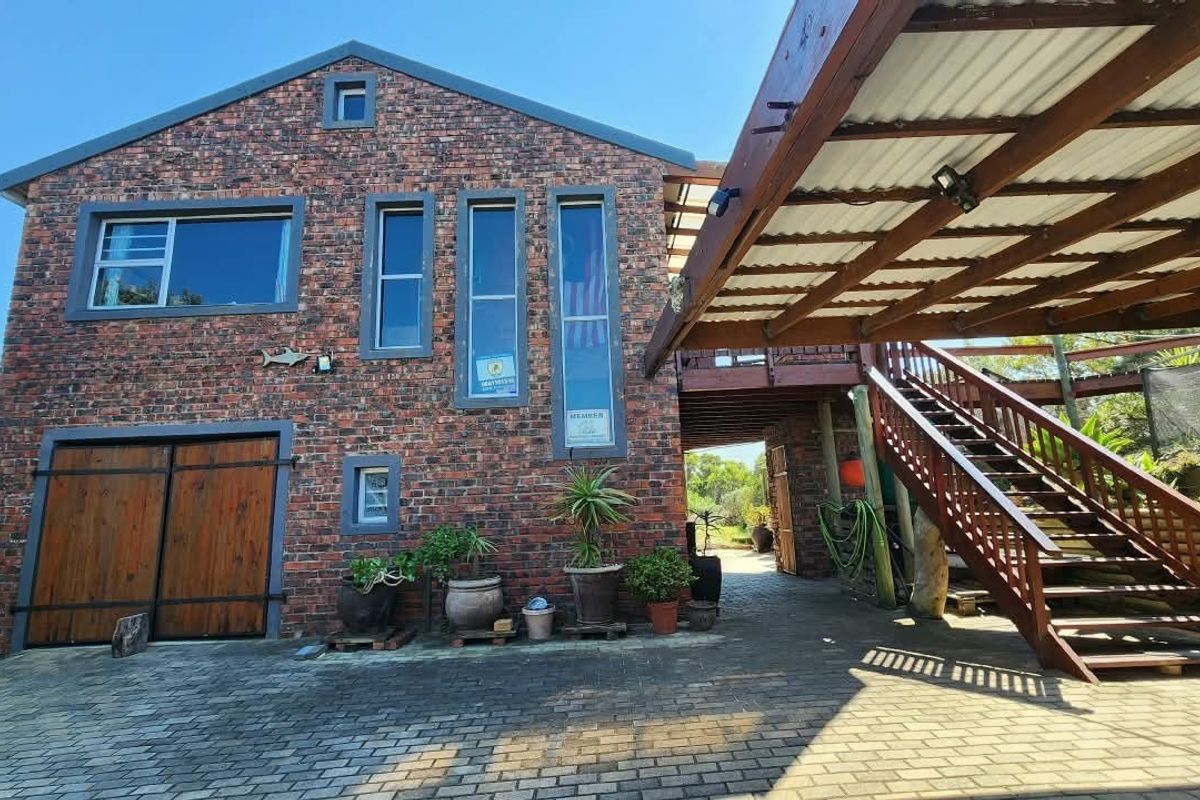 Rear exterior view featuring an exposed brick facade, timber garage doors, a covered timber staircase, and a paved driveway area.