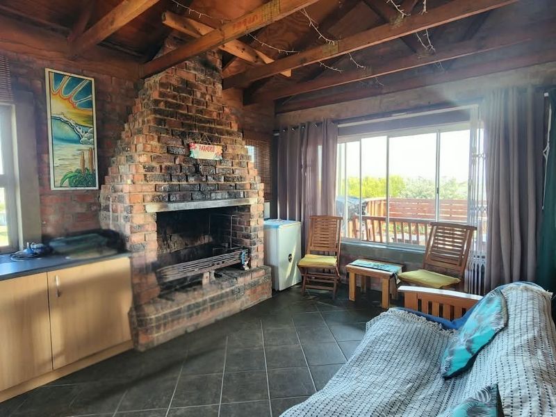 Rustic living area featuring an exposed timber beam ceiling, a prominent brick fireplace, tiled flooring, and sliding doors leading to an outdoor space.