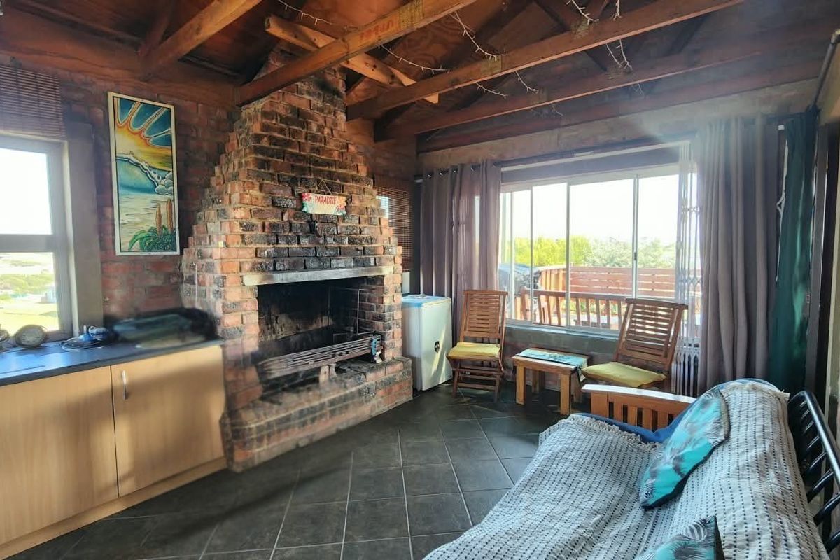 Rustic living area featuring an exposed timber beam ceiling, a prominent brick fireplace, tiled flooring, and sliding doors leading to an outdoor space.